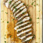 overhead shot of sliced, cooked turkey breast tenderloin on a wooden cutting board