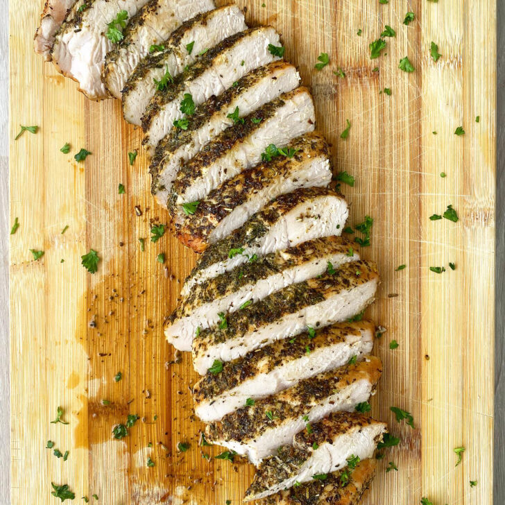 overhead shot of sliced, cooked turkey breast tenderloin on a wooden cutting board