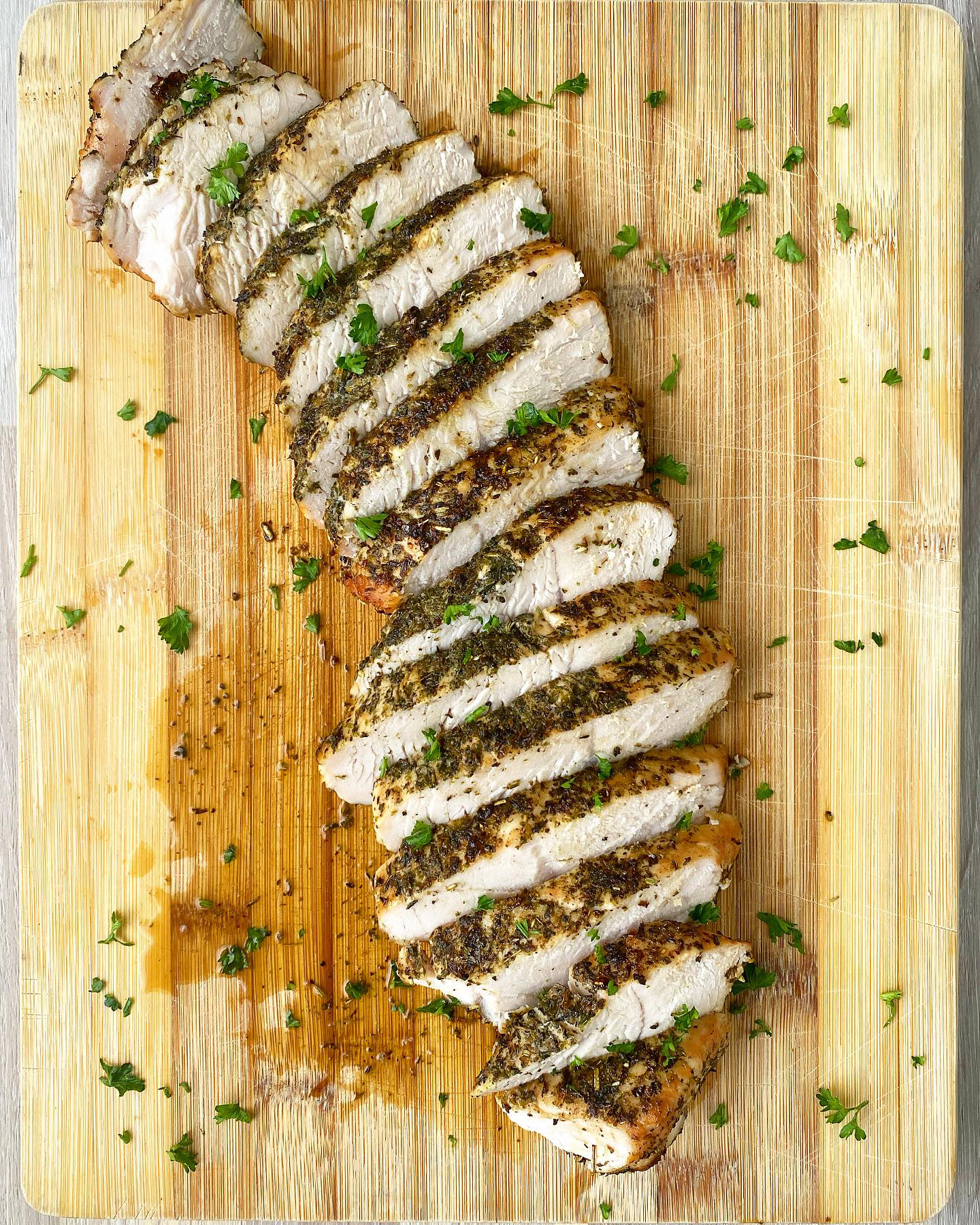 overhead shot of sliced, cooked turkey breast tenderloin on a wooden cutting board