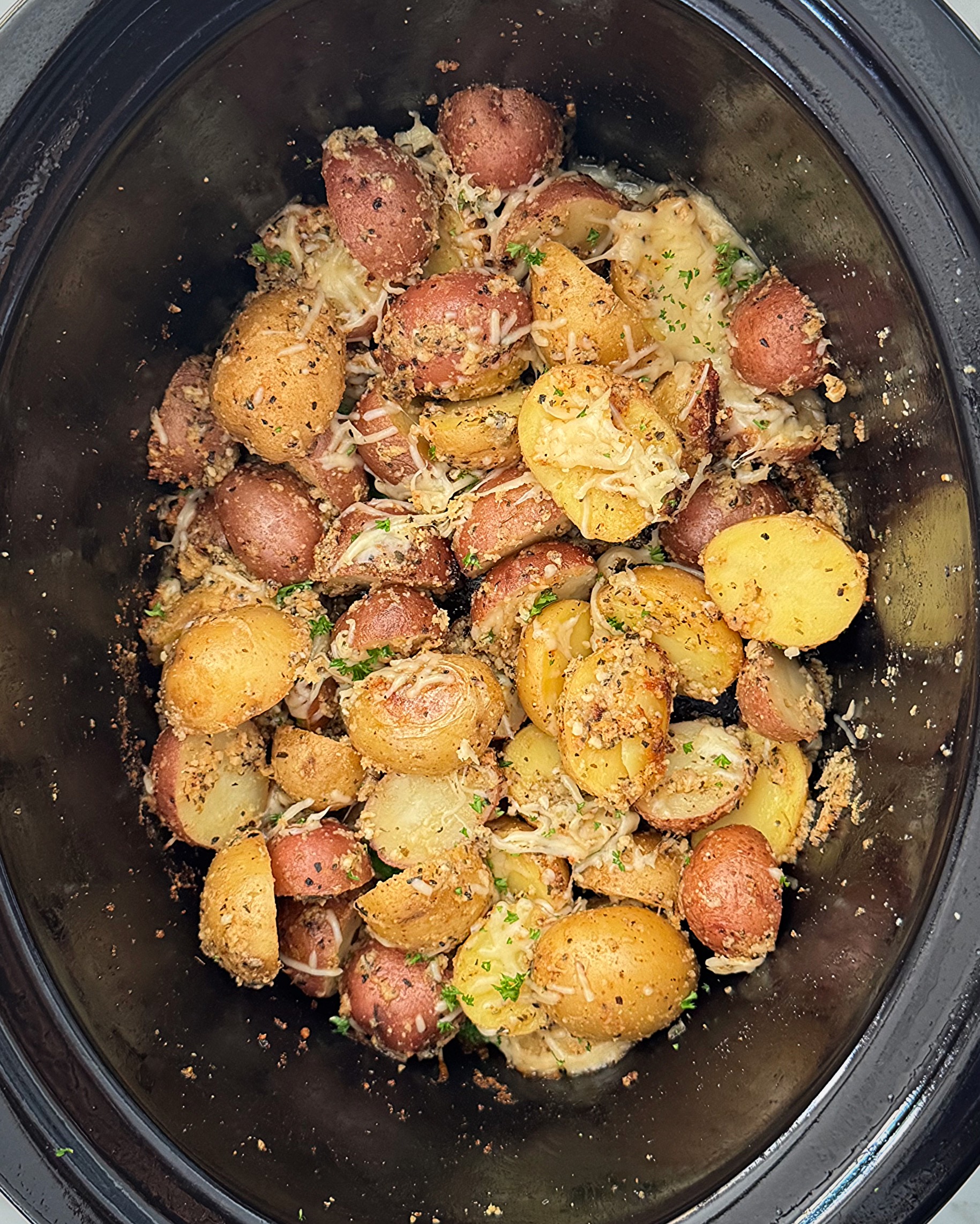 overhead shot of cooked Garlic Parmesan Potatoes in a black slow cooker