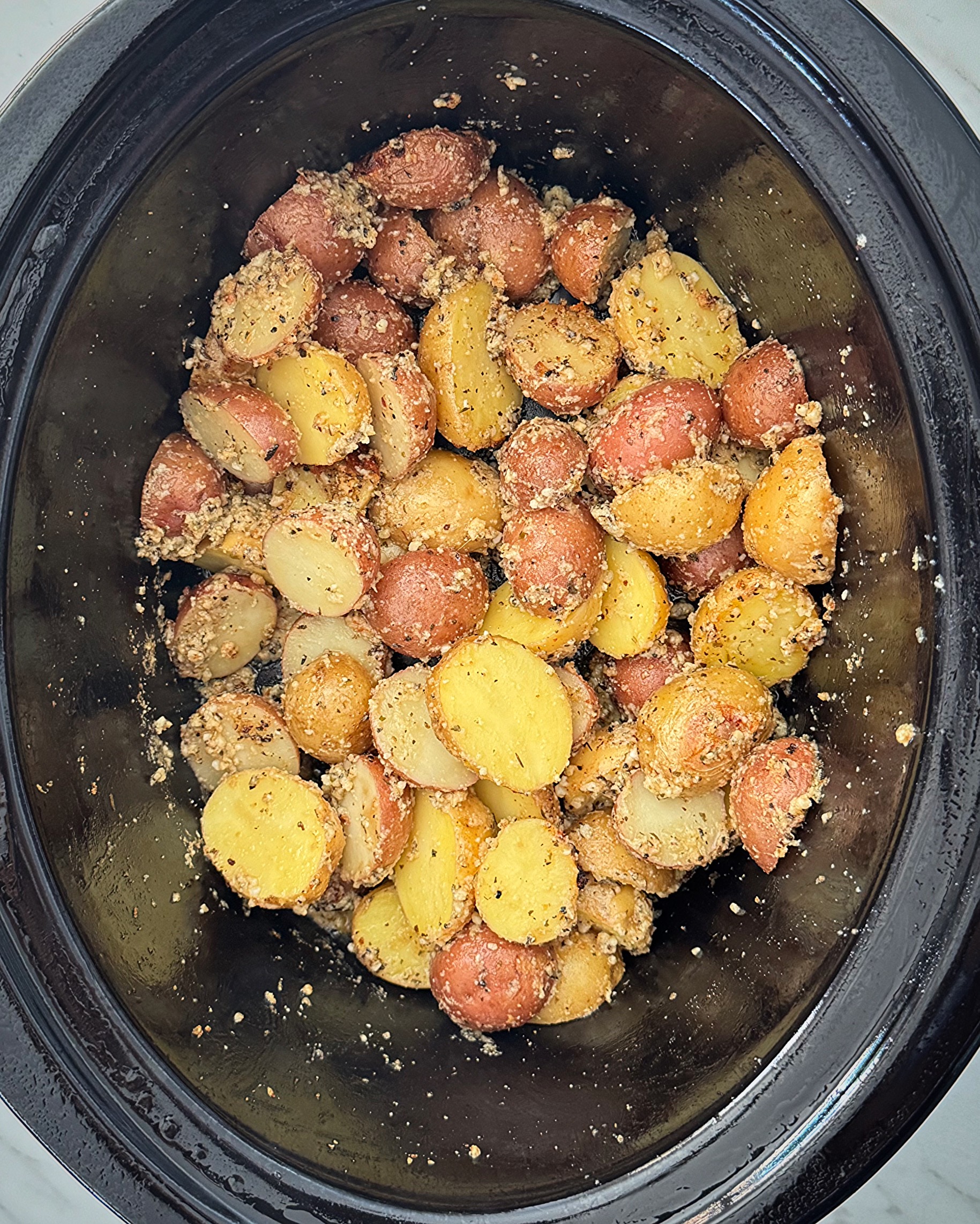 overhead shot of cooked Garlic Parmesan Potatoes in a black slow cooker