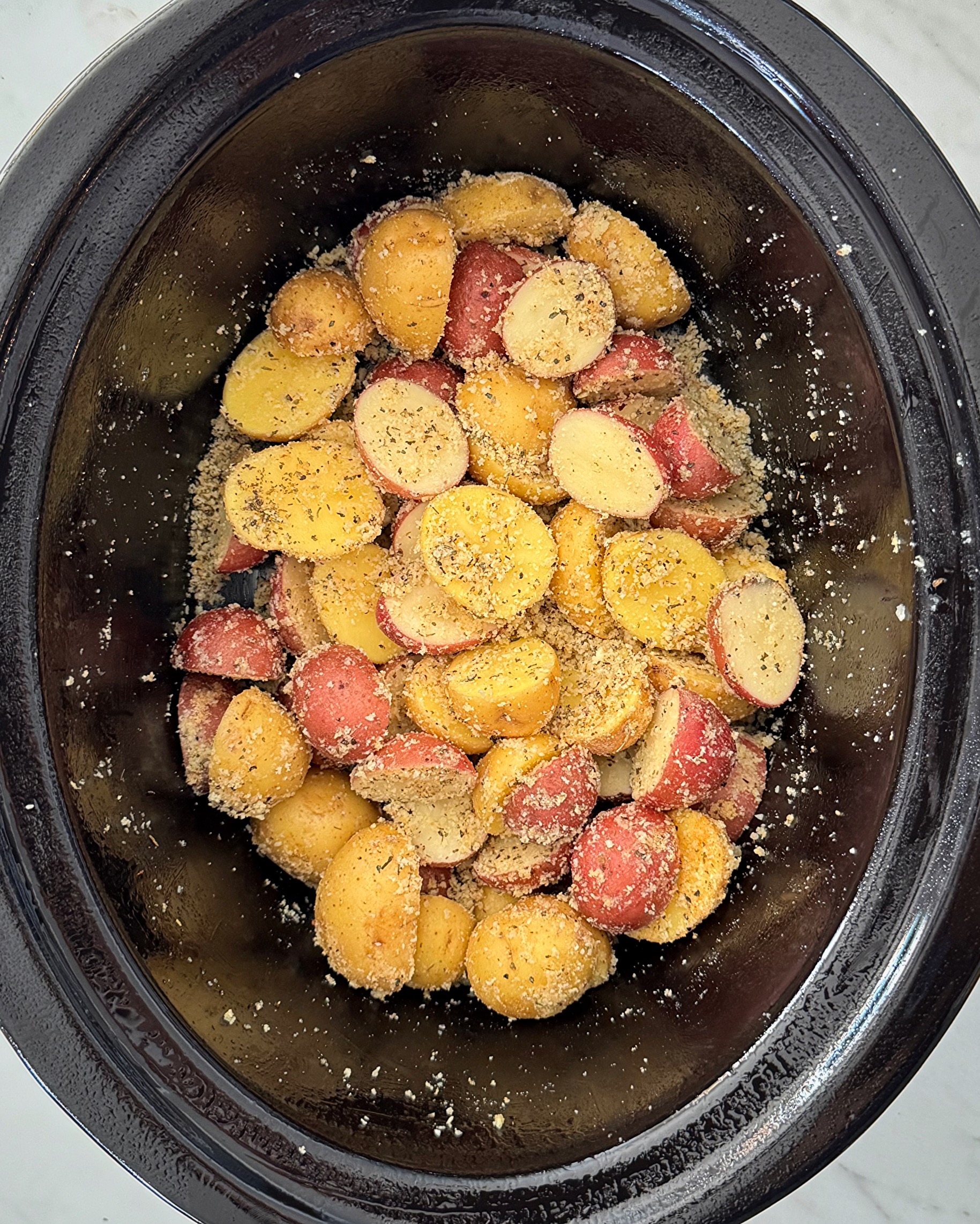 overhead shot of uncooked Garlic Parmesan Potatoes in a black slow cooker