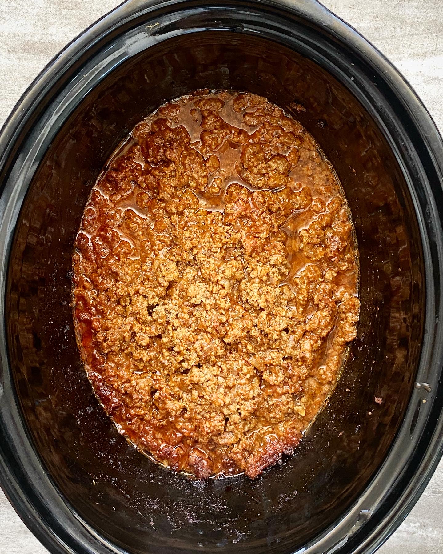 overhead shot of cooked hot dog chili sauce in a black slow cooker