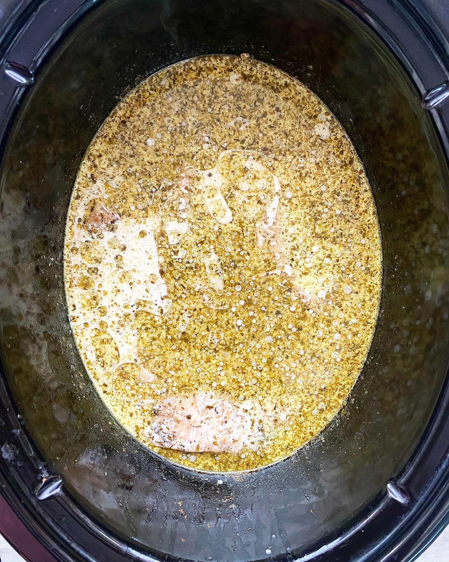 overhead shot of cooked pork chops in the a black slow cooker in a cream sauce