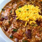 side view close up shot of pumpkin chili in a white bowl with a silver spoon