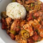 overhead shot of Crockpot Chicken Okra Tomatoes on a white plate with a cup of white rice