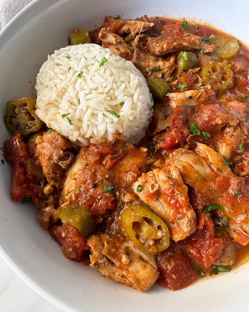 overhead shot of Crockpot Chicken Okra Tomatoes on a white plate with a cup of white rice