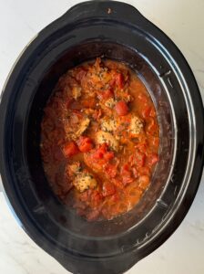 overhead shot of uncooked Chicken Okra Tomatoes in a black slow cooker