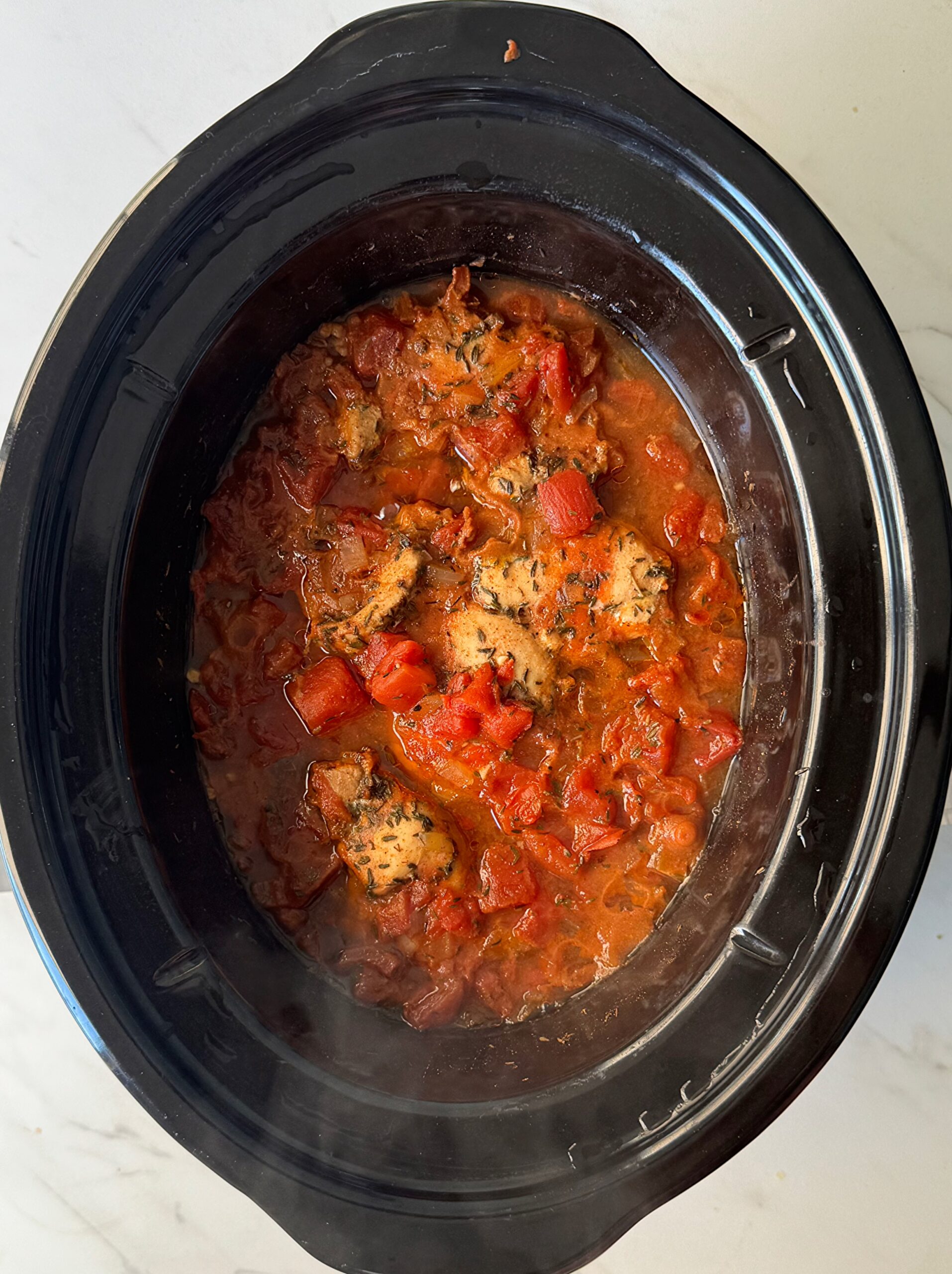 overhead shot of uncooked Chicken Okra Tomatoes in a black slow cooker