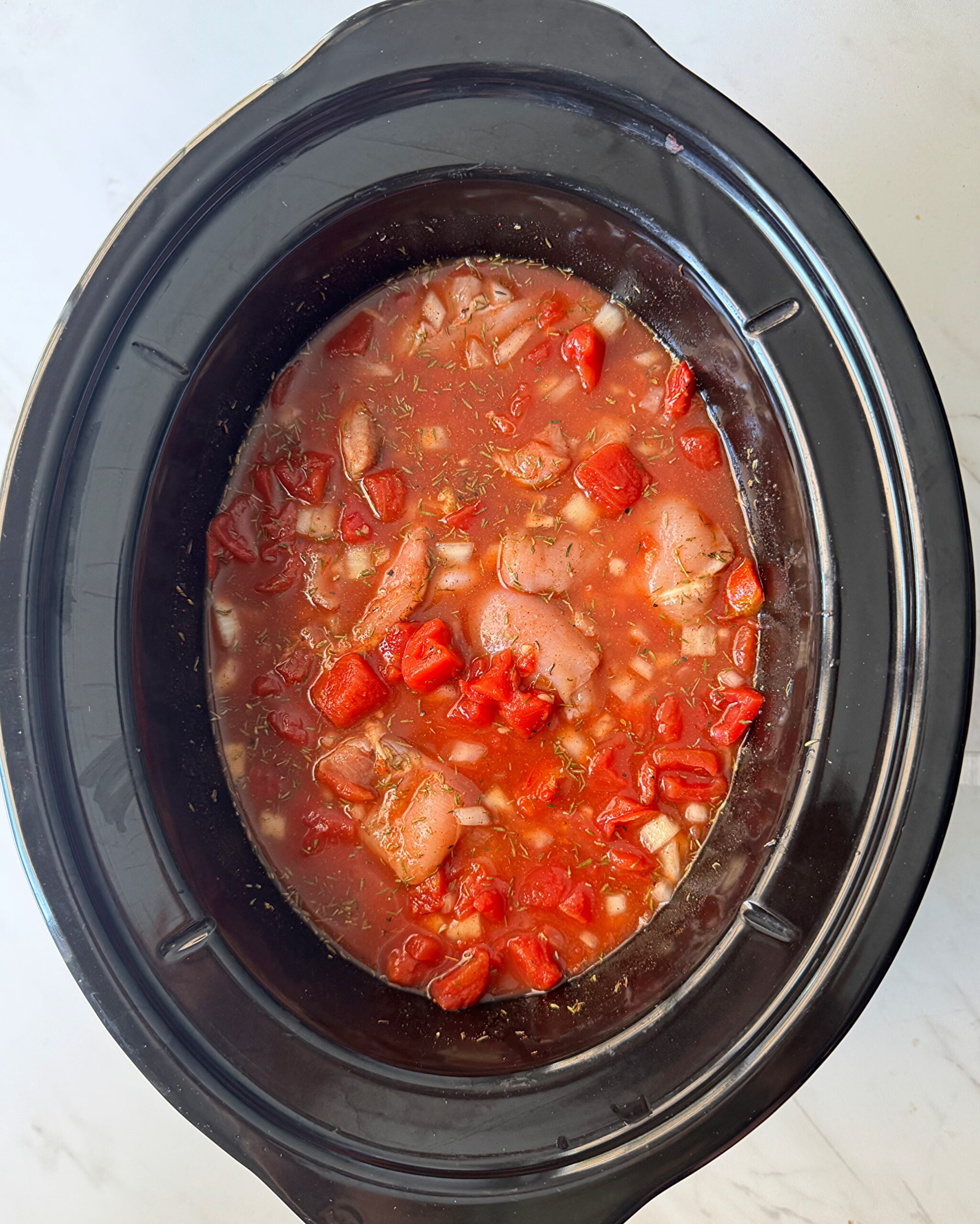 overhead shot of uncooked Chicken Okra Tomatoes in a black slow cooker