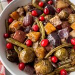 overhead shot of cooked harvest vegetables in a white bowl garnished with fresh cranberries