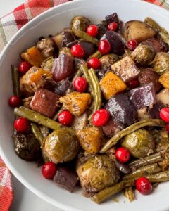 overhead shot of cooked harvest vegetables in a white bowl garnished with fresh cranberries