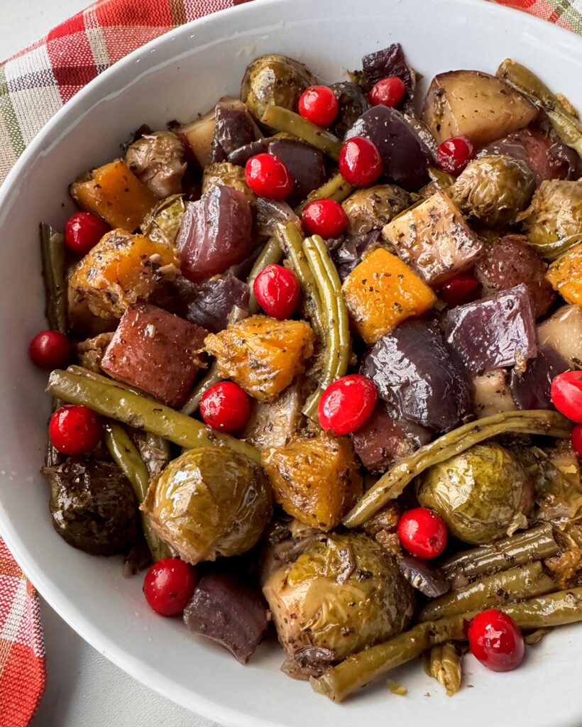 overhead shot of cooked harvest vegetables in a white bowl garnished with fresh cranberries