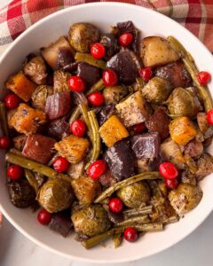 overhead shot of cooked harvest vegetables in a white bowl garnished with fresh cranberries