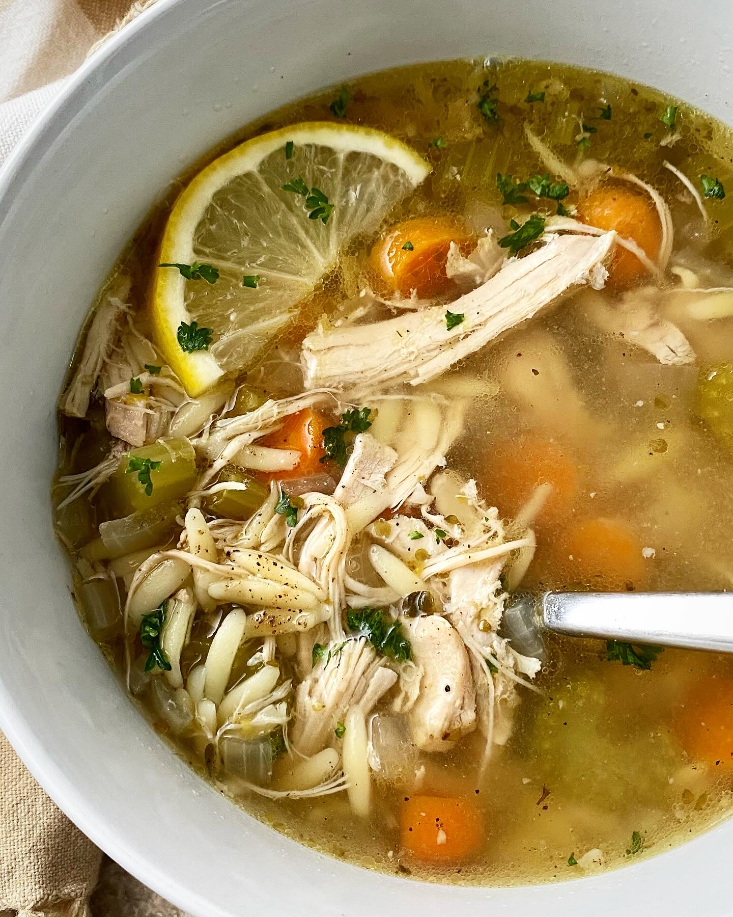 close up shot of lemon Chicken Orzo Soup in a white bowl garnished with a lemon slice