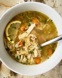 overhead shot of lemon Chicken Orzo Soup in a white bowl garnished with a lemon slice