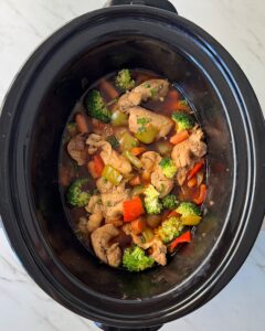 overhead shot of cooked chicken and vegetables in a black slow cooker