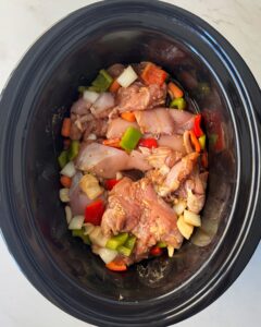 overhead shot of uncooked chicken and vegetables in a black slow cooker