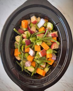 overhead shot of uncooked vegetables in a black slow cooker