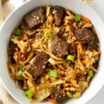 overhead shot of slow cooker teriyaki beef slaw in a white bowl garnished with sesame seeds and green onions
