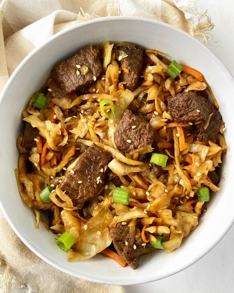overhead shot of slow cooker teriyaki beef slaw in a white bowl garnished with sesame seeds and green onions