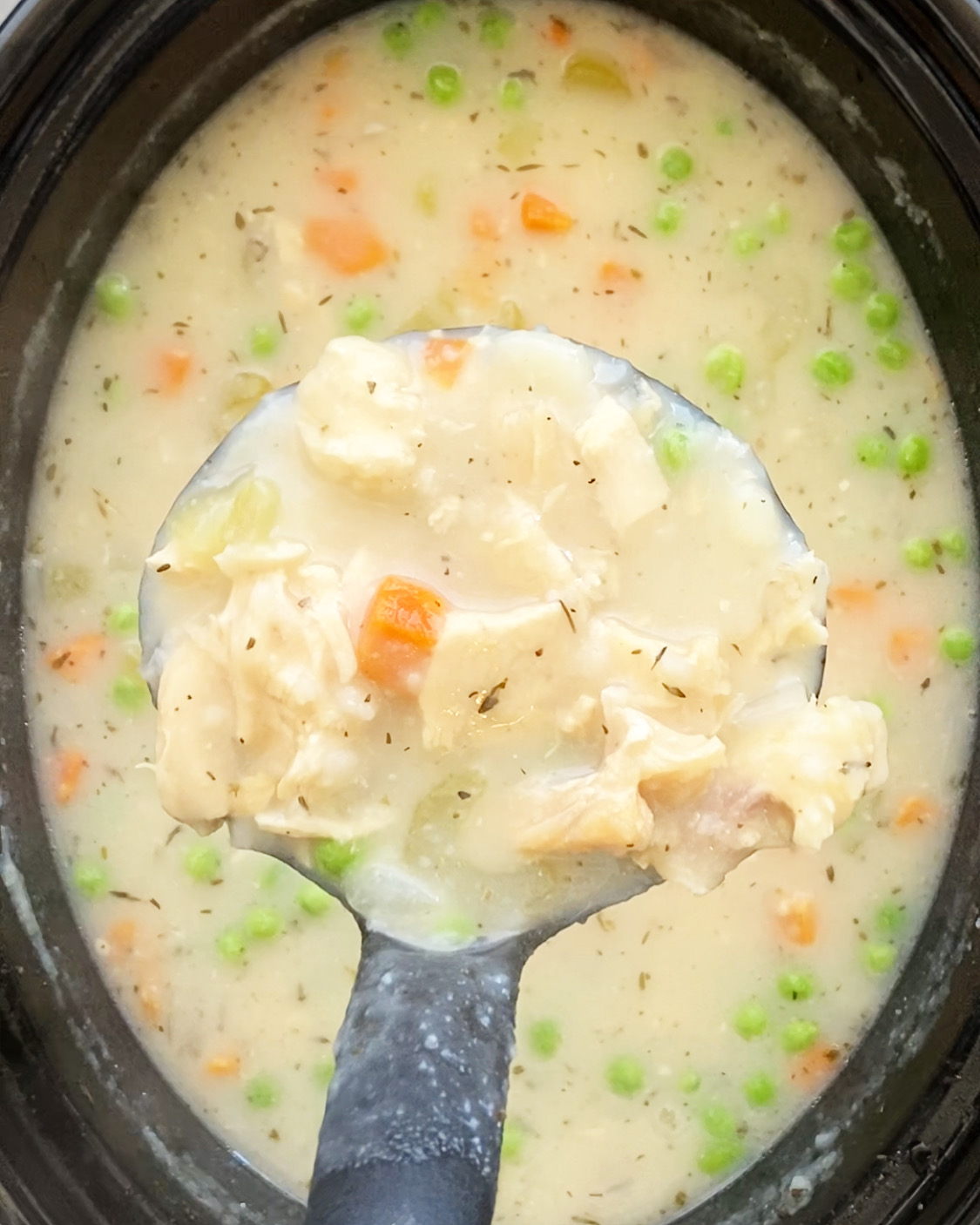 overhead shot of a large spoon of cooked turkey mashed potato soup over a in a black slow cooker