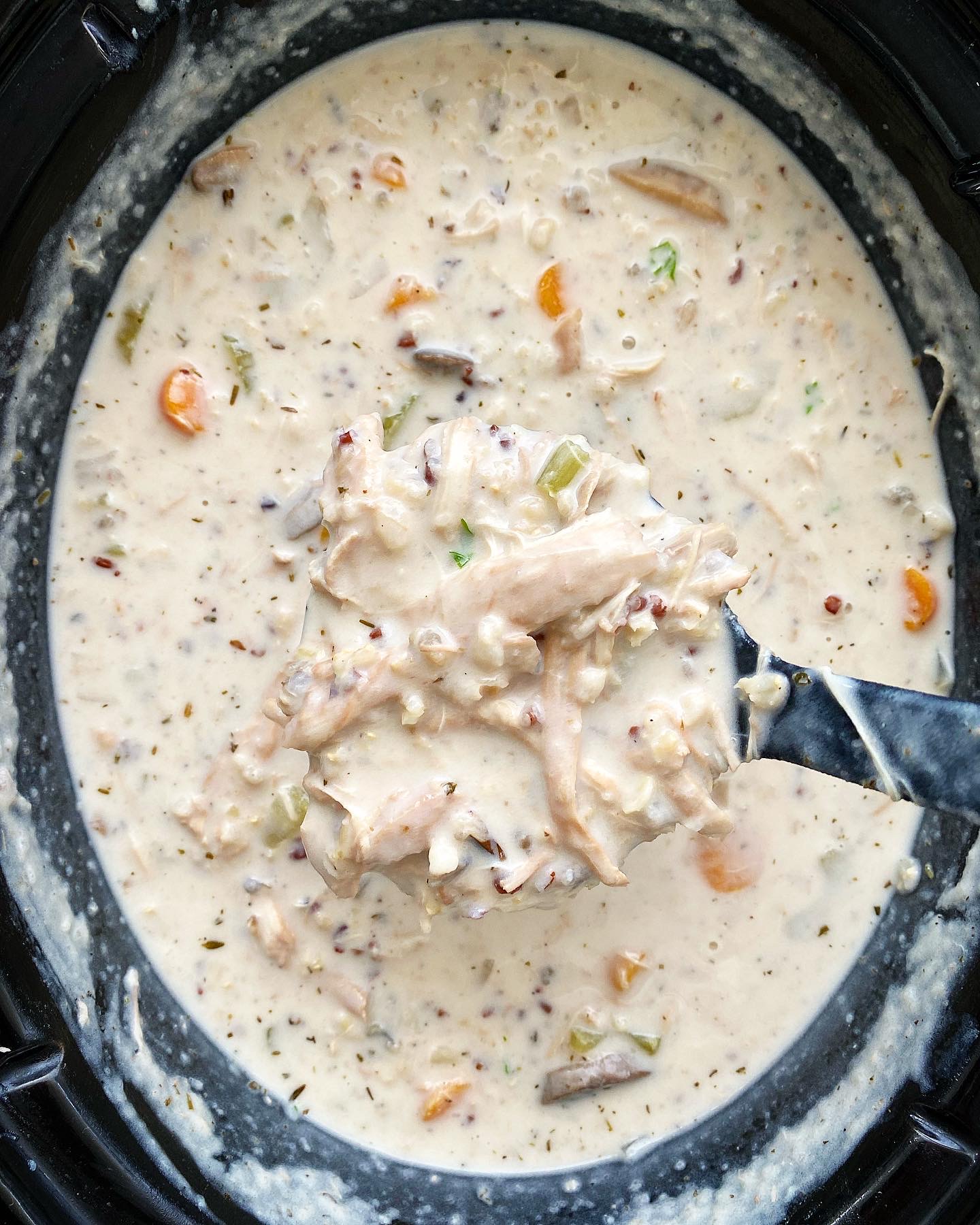 overhead shot of cooked Crockpot Turkey Wild Rice Soup in a black slow cooker with a black spoon scooping some out