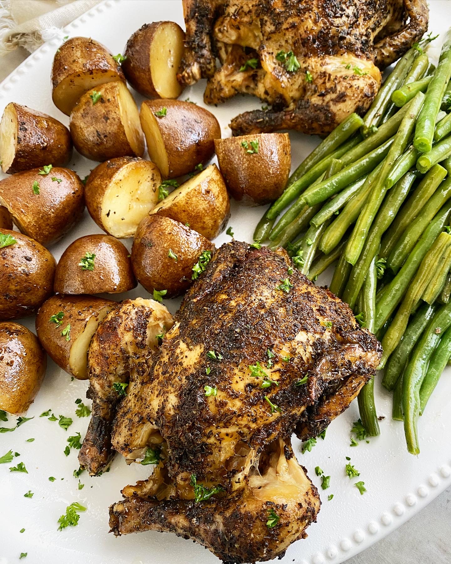 overhead, close up shot of cooked Cornish hens, potatoes, and green beans on a white platter
