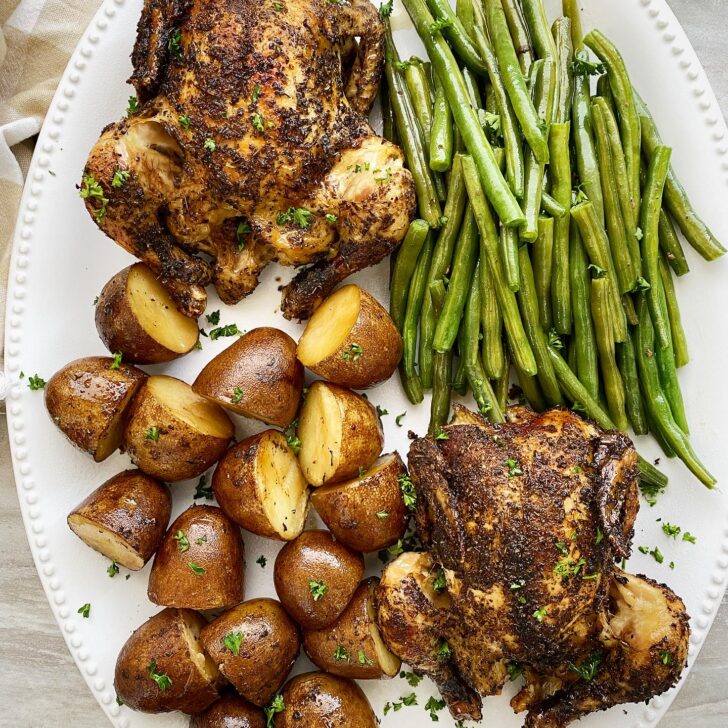 overhead shot of cooked Cornish hens, potatoes, and green beans on a white platter