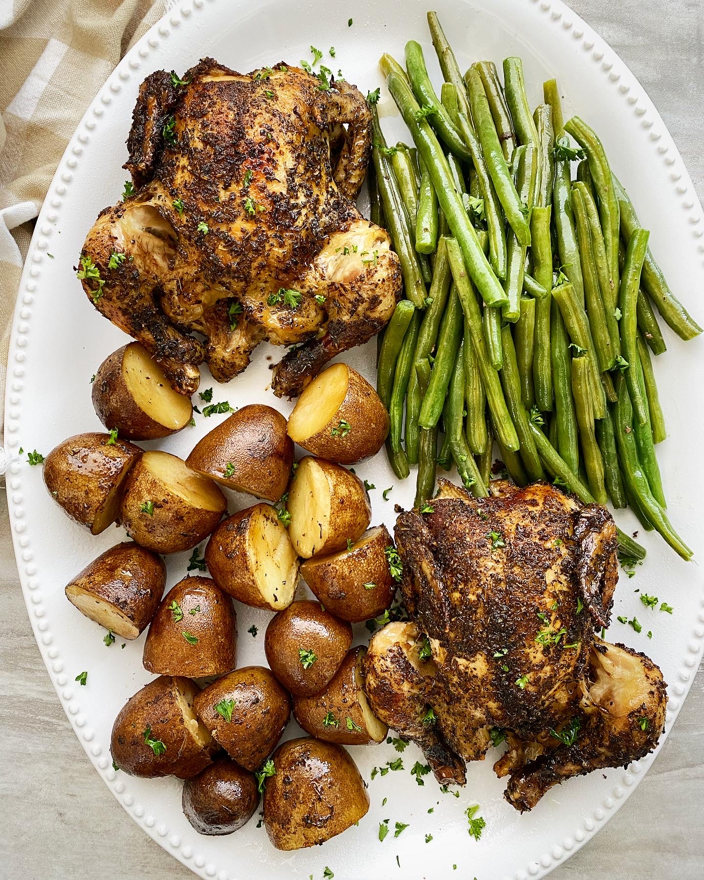 overhead shot of cooked Cornish hens, potatoes, and green beans on a white platter 