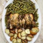 overhead shot of Cornish hens on a platter with green beans and sliced baby red potatoes