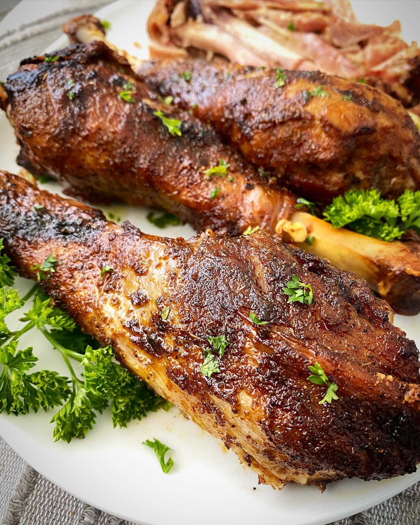 close up shot of slow cooker turkey legs on a white plate garnished with fresh parsley