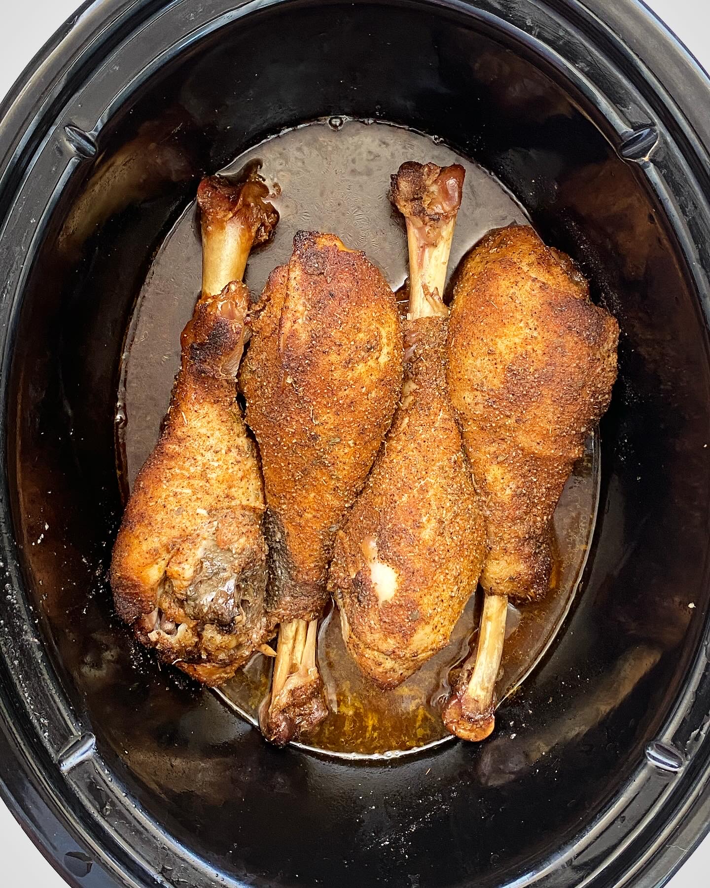 overhead shot of cooked turkey legs in a black slow cooker