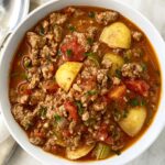 overhead shot of hamburger stew in a white bowl garnished with fresh parsley and a silver spoon
