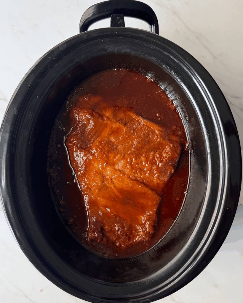 overhead shot of cooked BBQ brisket in a black slow cooker