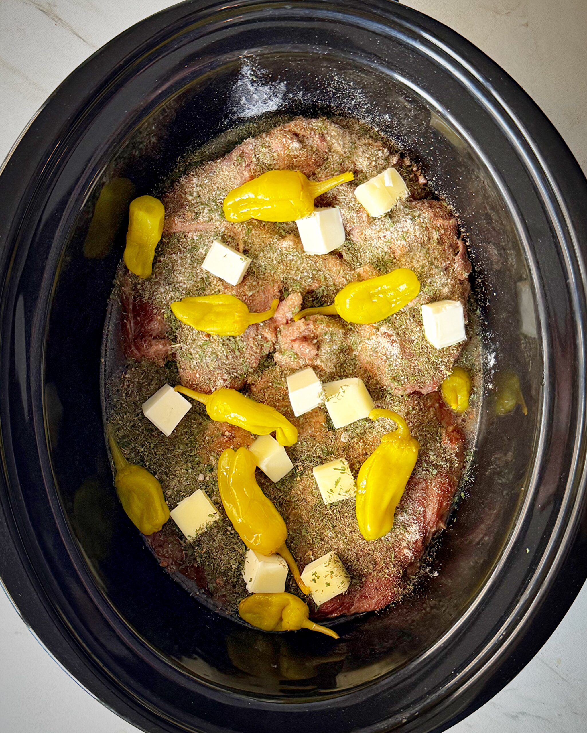 overhead shot of uncooked Mississippi Beef in a black slow cooker