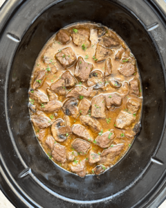 overhead shot of cooked garlic butter steak bites in a black slow cooker