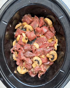 overhead shot of uncooked garlic butter steak bites in a black slow cooker