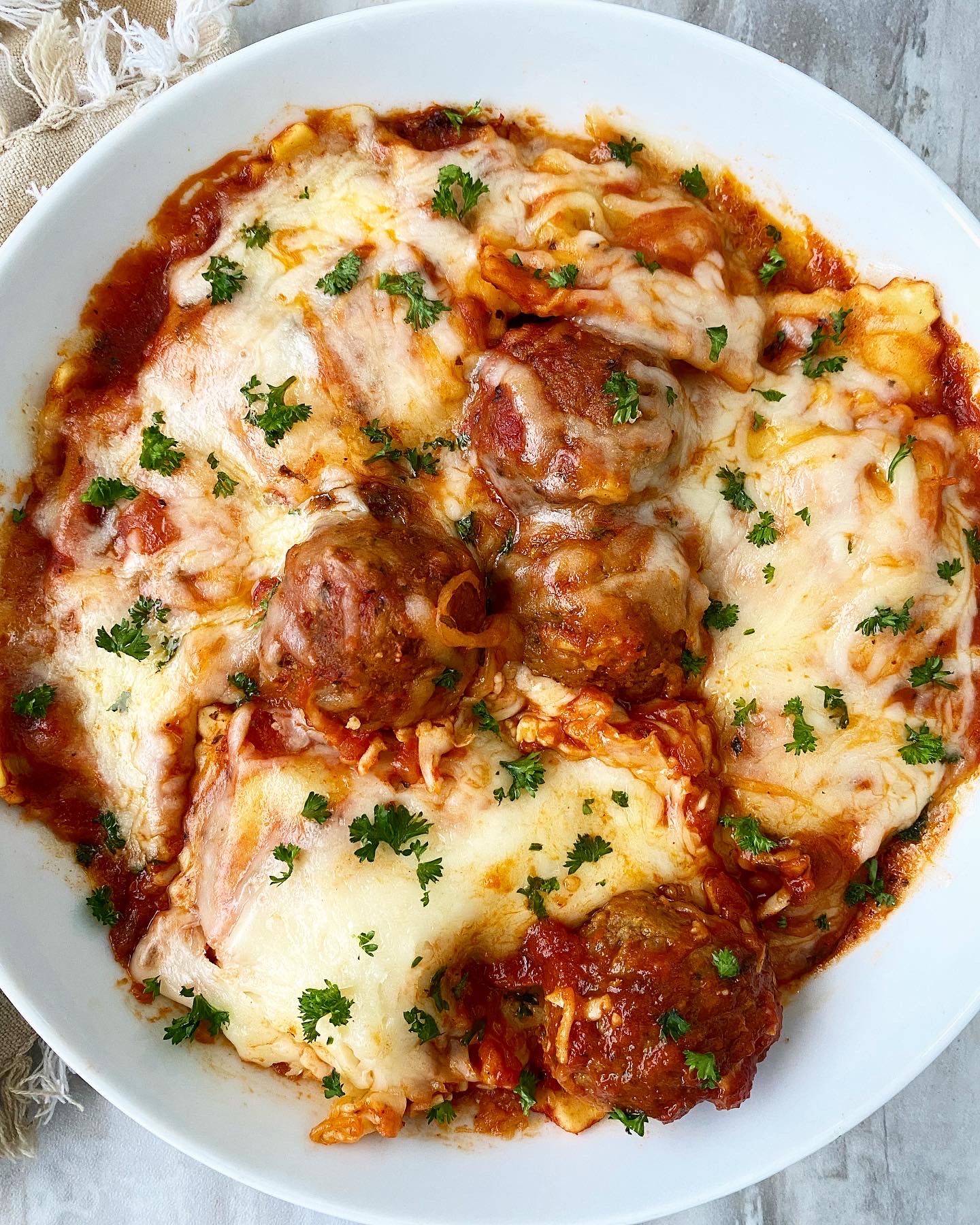 cooked Cheesy Ravioli Meatball Casserole in the slow cooker with parsley in a white bowl