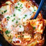 side close-up of cooked Cheesy Ravioli Meatball Casserole in the slow cooker with parsley with a meatball scooped out