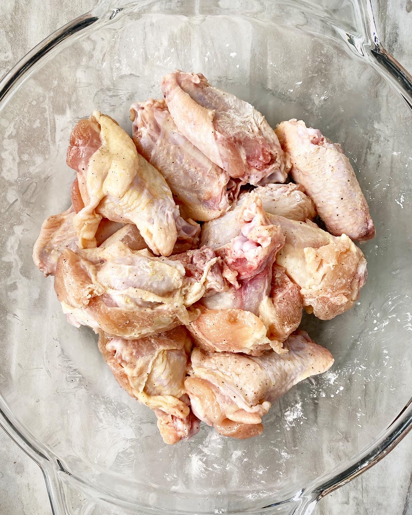 raw chicken wings in a clear bowl seasoned with salt, pepper, and arrowroot flour