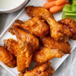 close up of air fryer buffalo chicken wings on a white plate with celery, carrots, and ranch dipping sauce