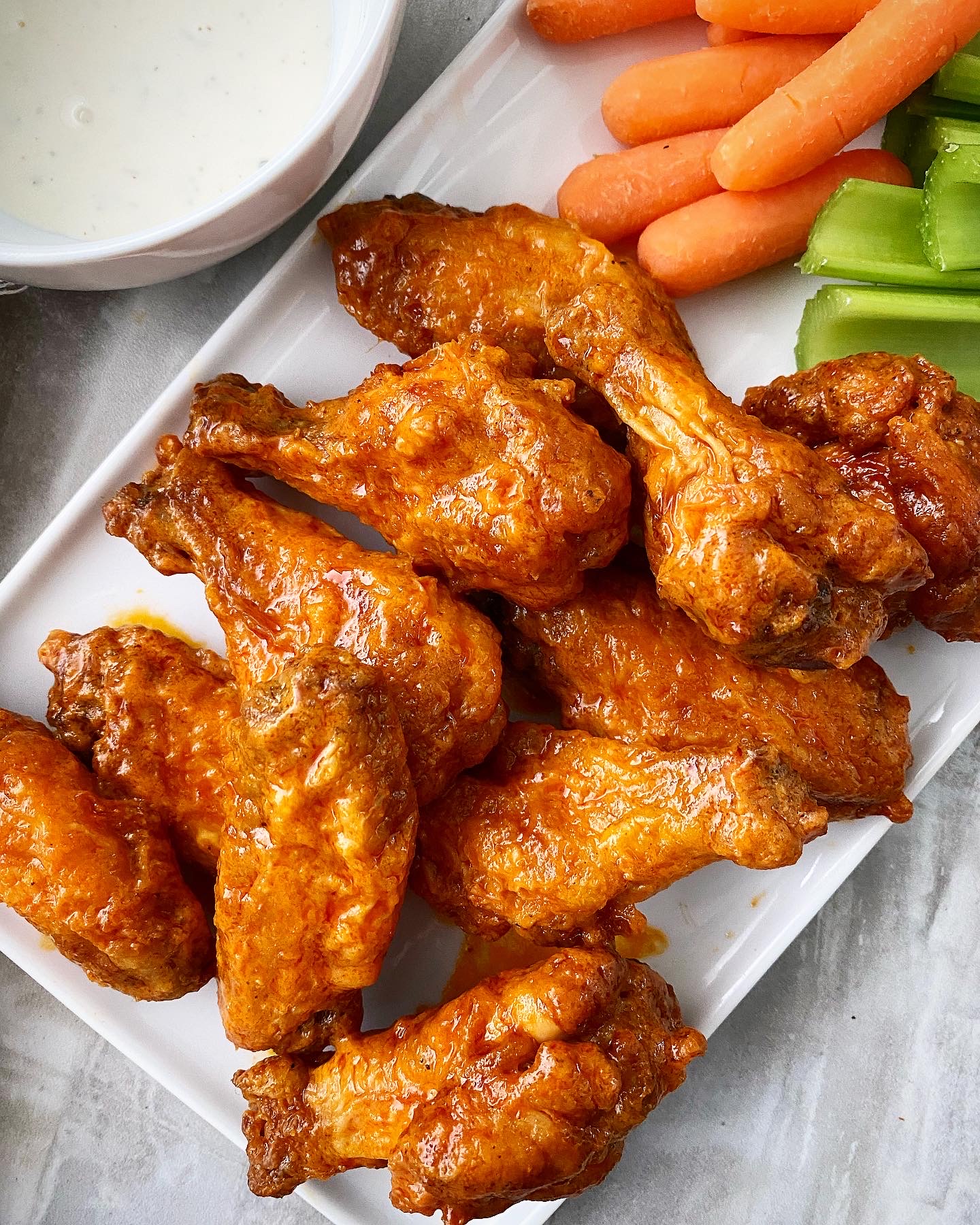 close up of air fryer buffalo chicken wings on a white plate with celery, carrots, and ranch dipping sauce