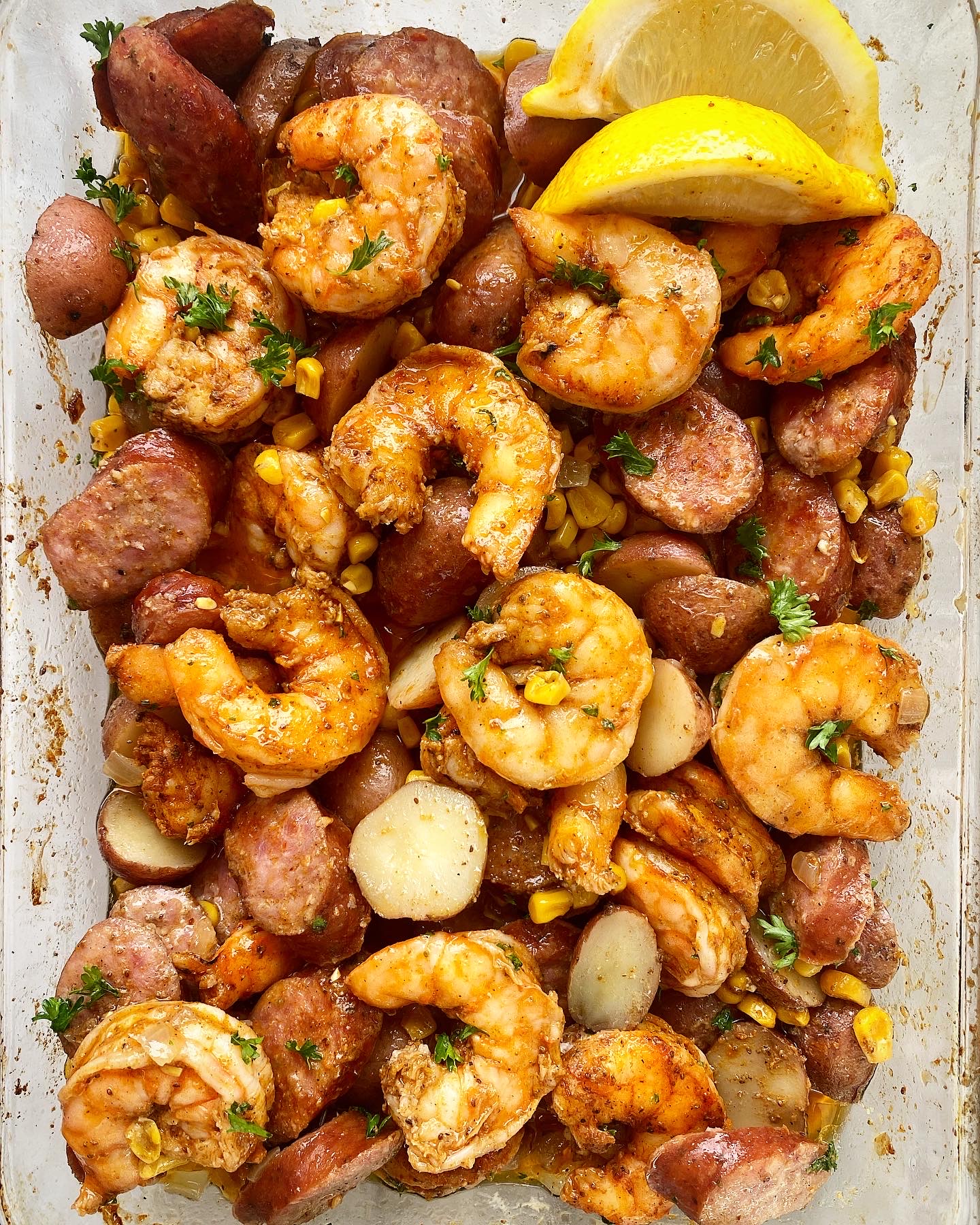shrimp boil casserole mixed up in a baking dish with lemon wedges