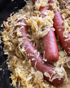 close of shot of cooked hot dogs in a black slow cooker covered in sauerkraut