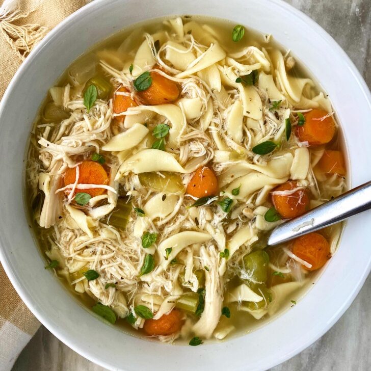 overhead shot of chicken noodle soup in a bowl with a silver spoon
