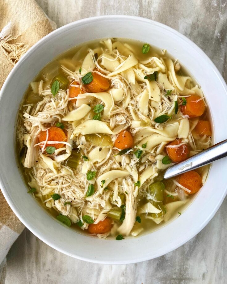 overhead shot of chicken noodle soup in a bowl with a silver spoon