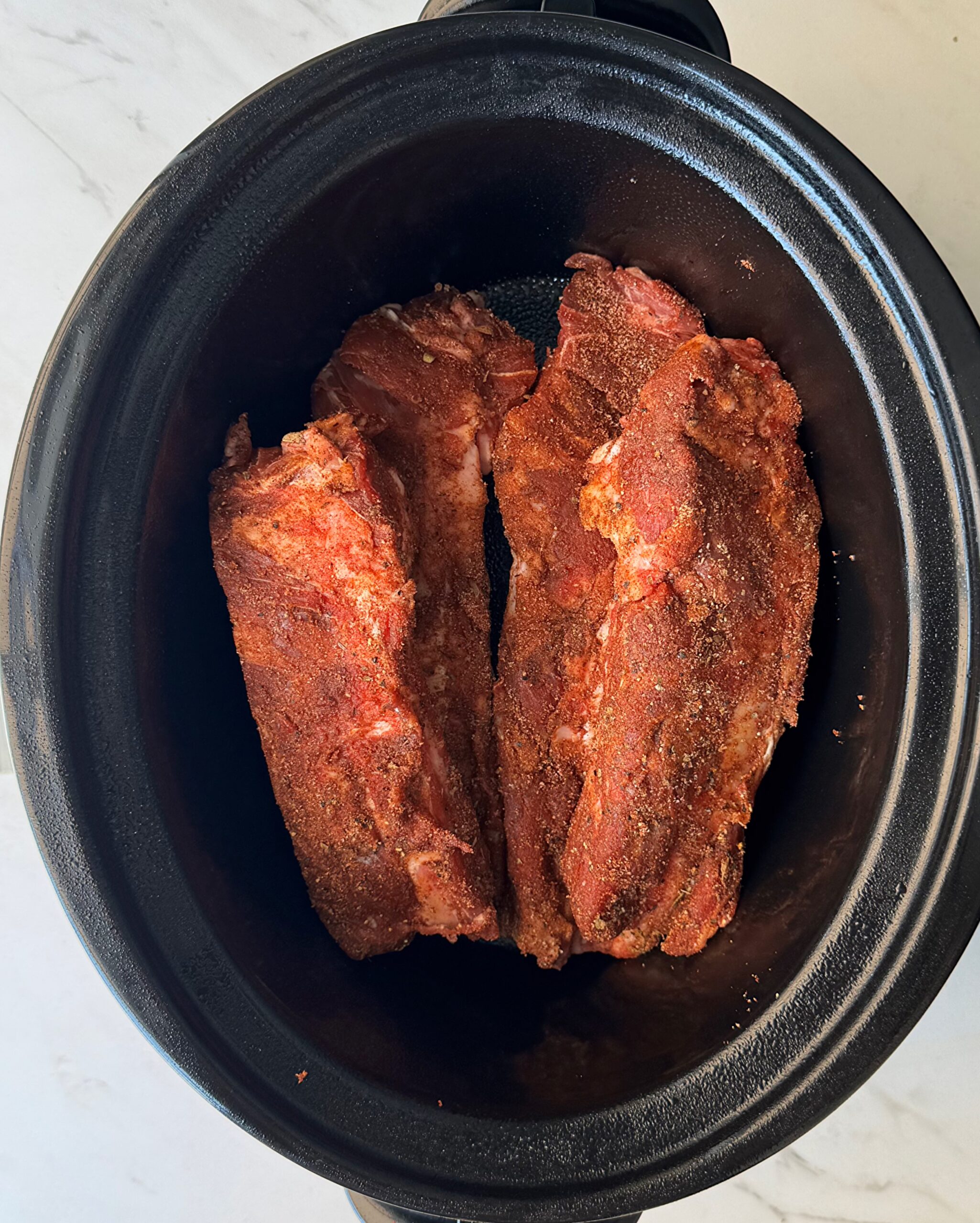 overhead shot of cooked beef back ribs in a black slow cooker