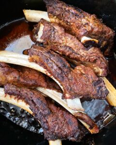 side shot of cooked, seasoned beef ribs in a black slow cooker