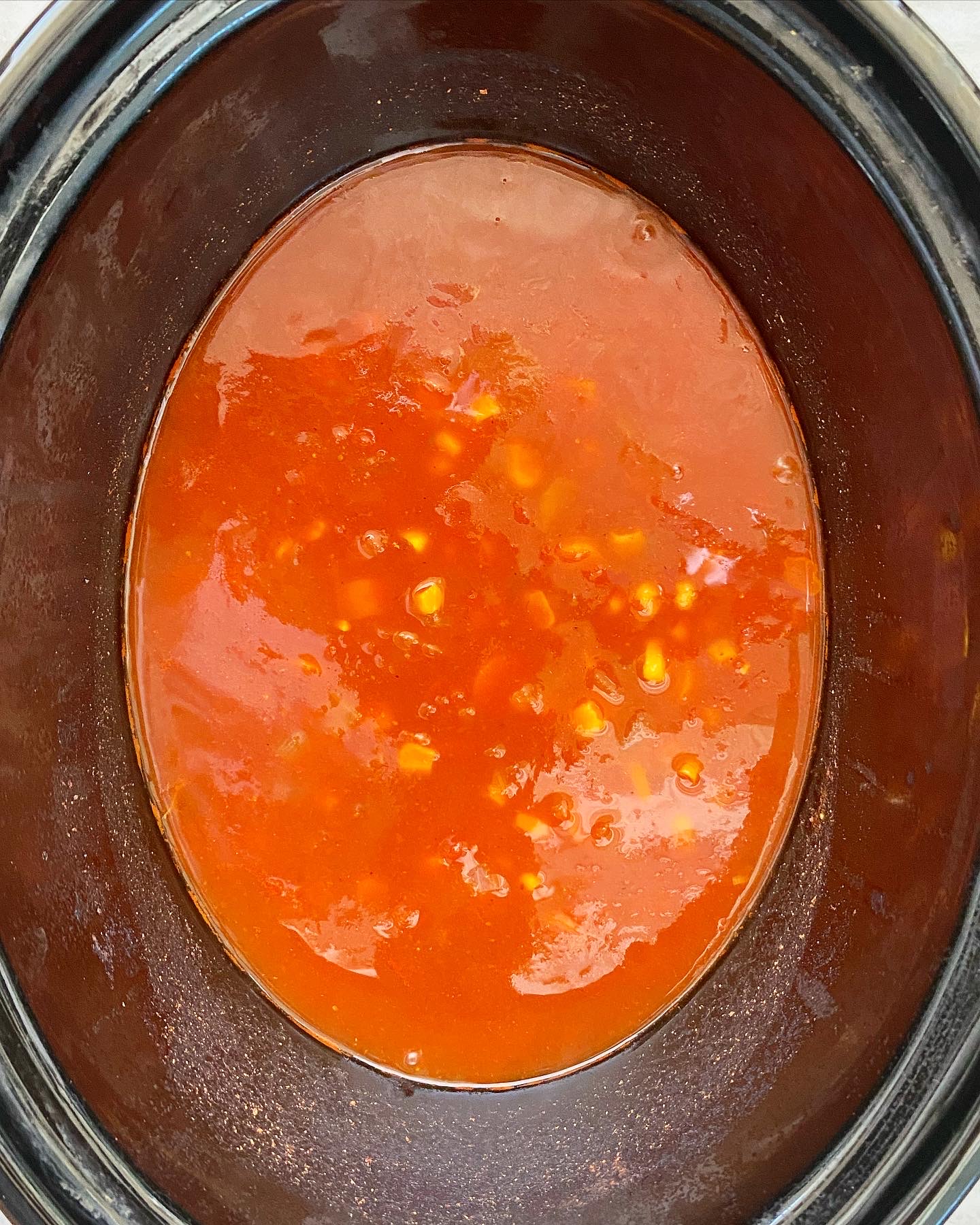 overhead shot of uncooked crab soup in a black slow cooker